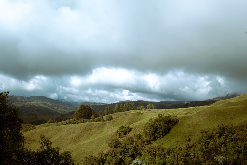 a cloudy sky over a green hillside with trees