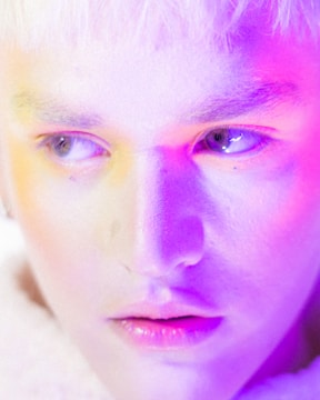 Close-up of a model bathed in soft purple lighting, highlighting textures and expressions.