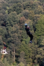 a man riding a zip line over a lush green forest