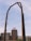 A large industrial structure, possibly for electrical wiring, is set against a partly cloudy sky. In the background, there is a multi-story brick building with a sign on top and various other industrial elements.