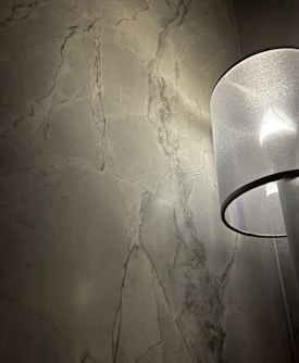 A textured, dark grey stone wall with visible veining patterns. On the right side, a modern, translucent lampshade emits a soft light that highlights the wall texture.