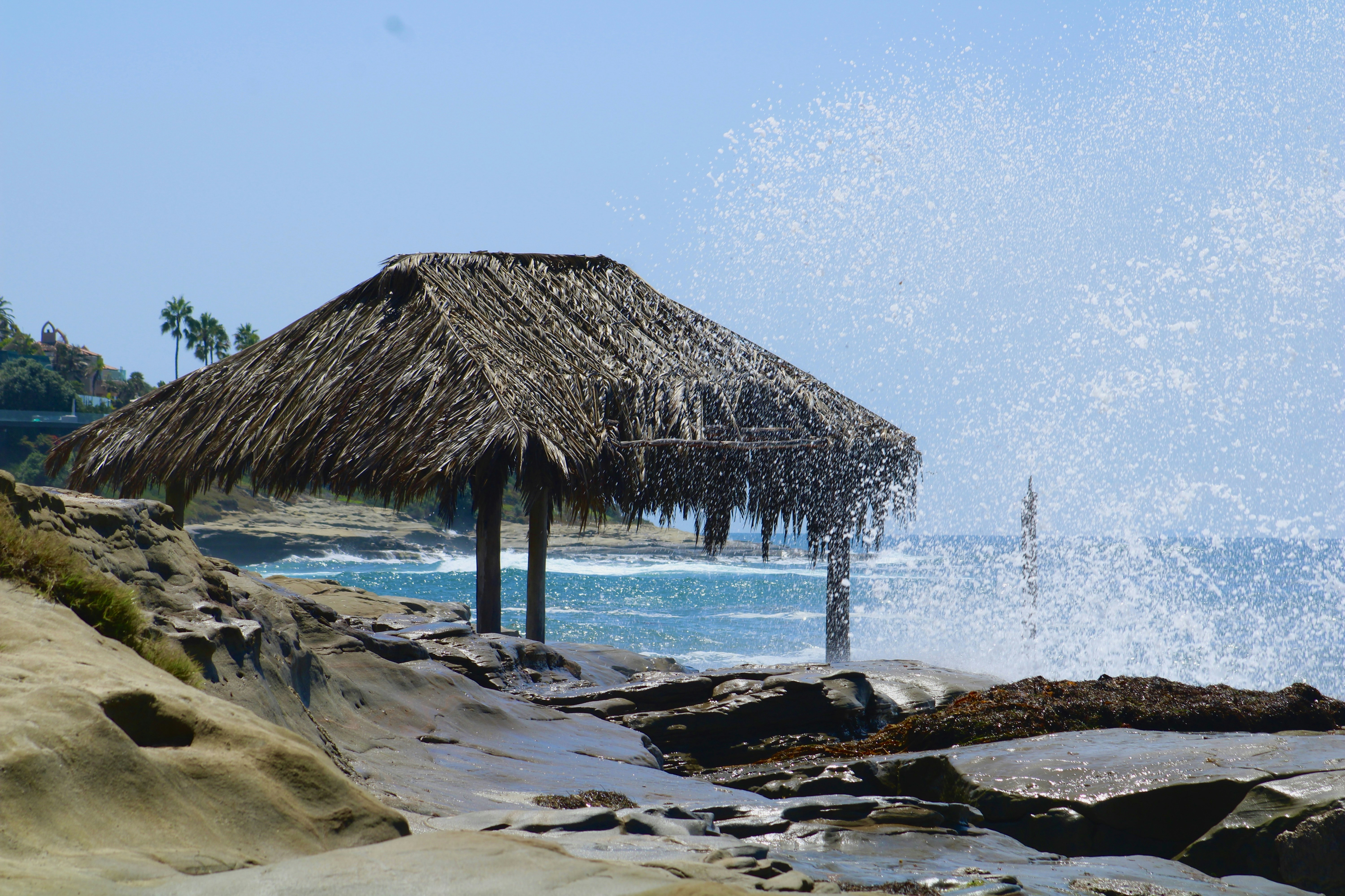 a thatched hut on a rocky beach next to the ocean