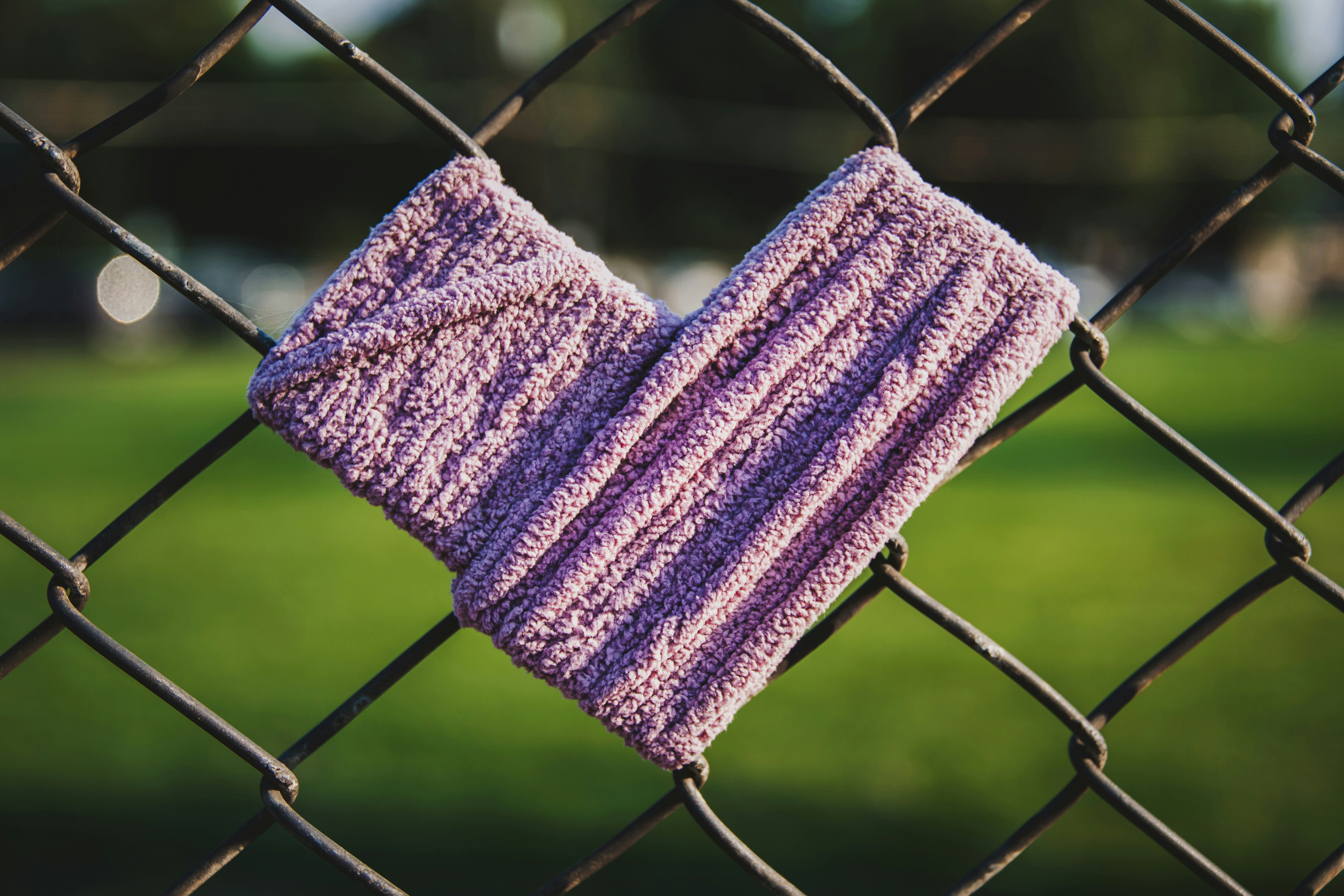 a pair of purple mitts hanging on a chain link fence