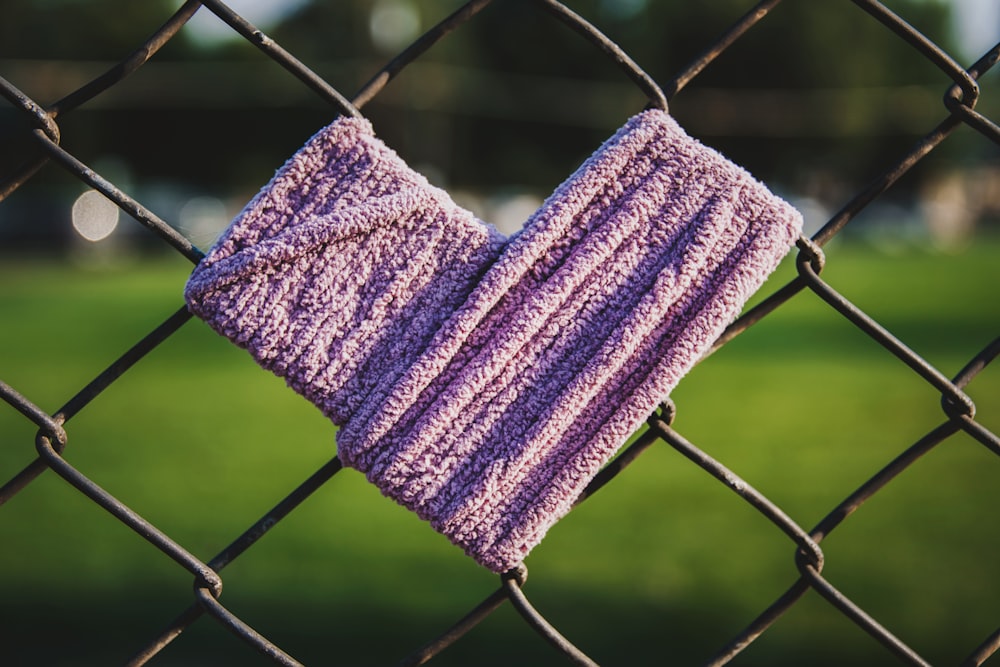 ein Paar lila Handschuhe, die an einem Maschendrahtzaun hängen