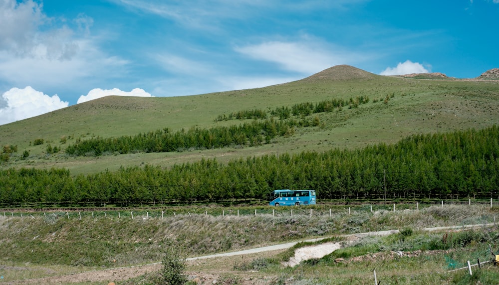 a blue train traveling through a lush green hillside