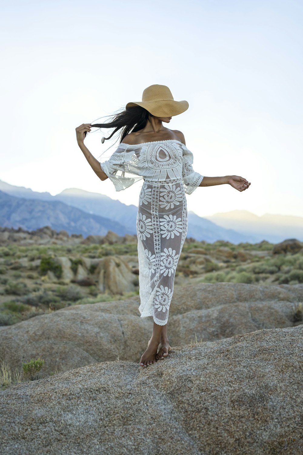 a woman in a white dress and hat walking on a rock