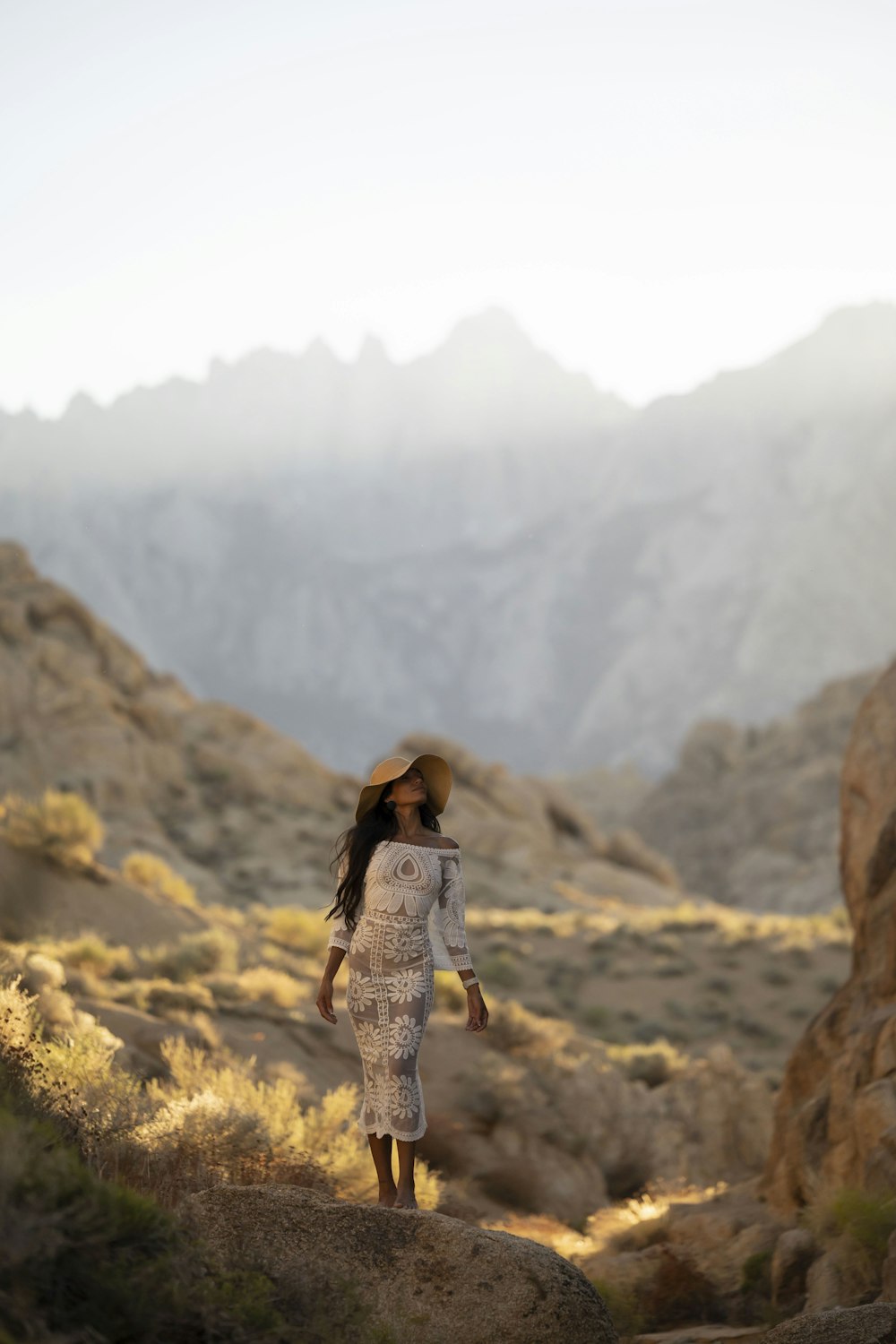 a woman in a white dress walking on a rocky hillside