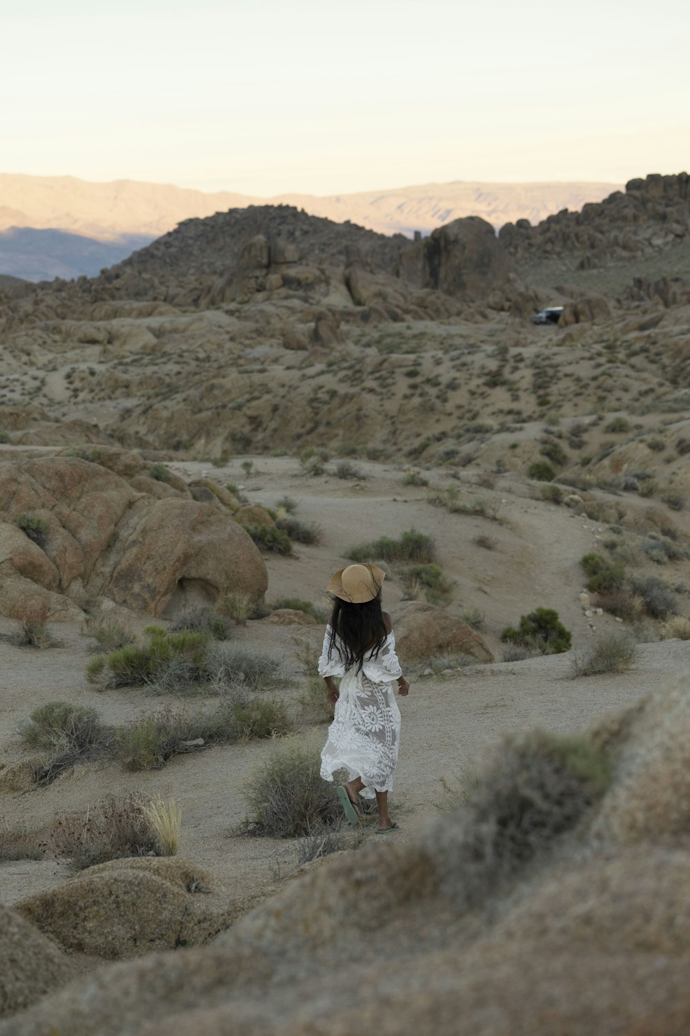 a woman in a white dress and hat walking through the desert