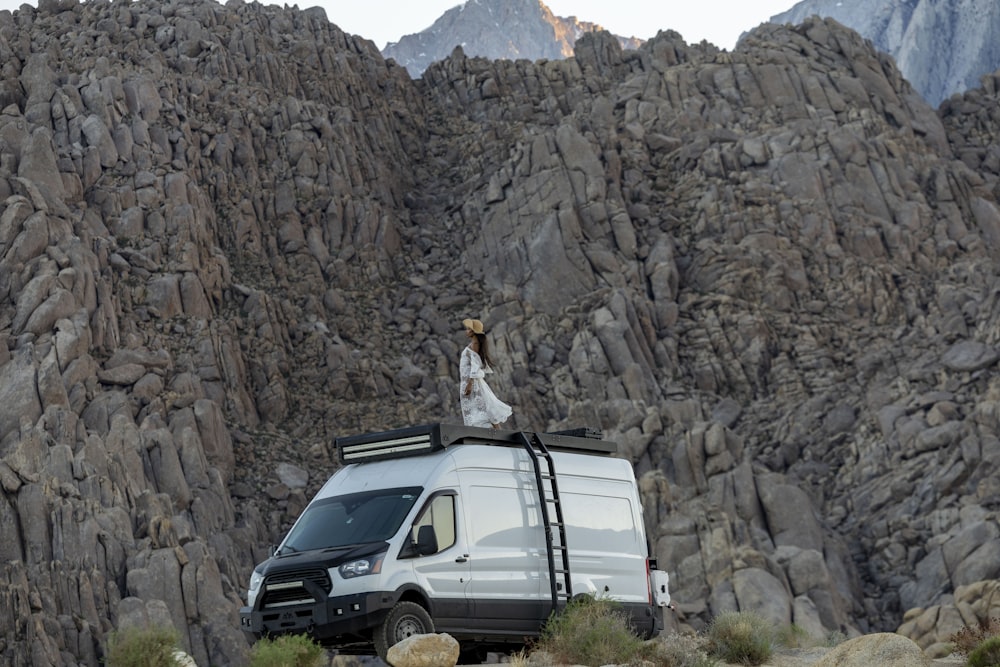a woman standing on top of a van in the mountains