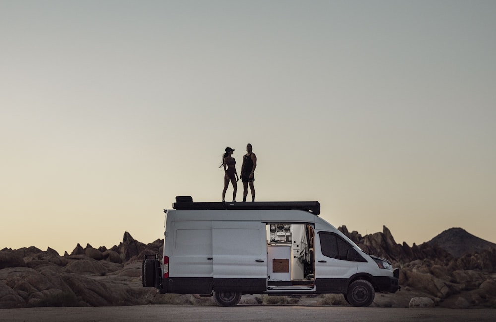 two people standing on top of a van