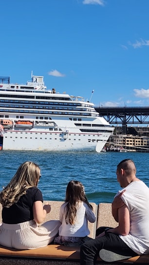 A happy family boarding a cruise ship with luggage, smiling under a bright blue sky.