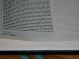 A close-up of a page from an open book, containing text with a religious theme. The text is printed in a serif font and includes numbered verses. The page has annotations or footnotes at the bottom.
