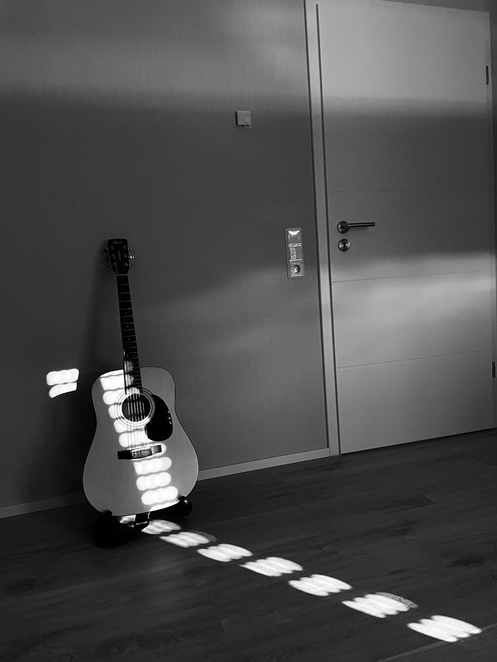 Una foto in bianco e nero di una chitarra appoggiata a un muro