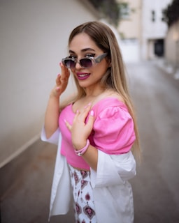 Indian female model smiling brightly in stylish pink-tinted sunglasses on a sunny street.