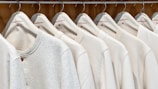 A row of identical light-colored sweaters is neatly hung on wooden hangers against a wooden background. Each sweater has a simple design with a round neckline and is labeled with the size 'M' and the brand 'Vintage Republic'. The arrangement is orderly, creating a sense of uniformity.