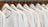A row of identical light-colored sweaters is neatly hung on wooden hangers against a wooden background. Each sweater has a simple design with a round neckline and is labeled with the size 'M' and the brand 'Vintage Republic'. The arrangement is orderly, creating a sense of uniformity.