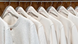 A row of identical light-colored sweaters is neatly hung on wooden hangers against a wooden background. Each sweater has a simple design with a round neckline and is labeled with the size 'M' and the brand 'Vintage Republic'. The arrangement is orderly, creating a sense of uniformity.