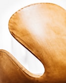 A close-up view of a sleek, curved chair with a light tan, leather-like texture, highlighting its elegant design against a bright white background.