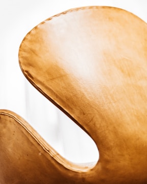 A close-up view of a sleek, curved chair with a light tan, leather-like texture, highlighting its elegant design against a bright white background.