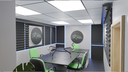 A modern podcast studio with professional microphone setups on a table surrounded by green and black office chairs. The room has acoustic foam on the walls for soundproofing and large square ceiling lights. The walls are predominantly adorned with decorative panels and some branding elements.