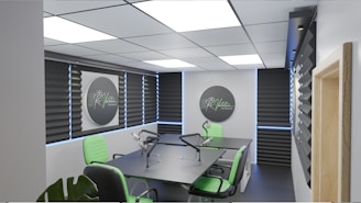 A modern podcast studio with professional microphone setups on a table surrounded by green and black office chairs. The room has acoustic foam on the walls for soundproofing and large square ceiling lights. The walls are predominantly adorned with decorative panels and some branding elements.