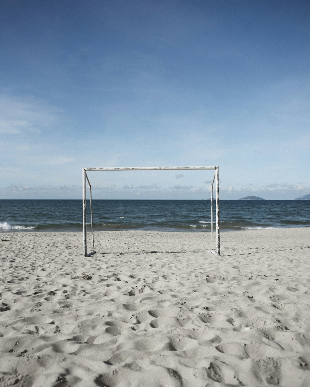 a soccer goal on a beach with the ocean in the background