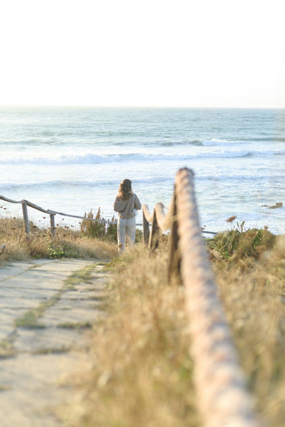 a woman walking down a path next to the ocean