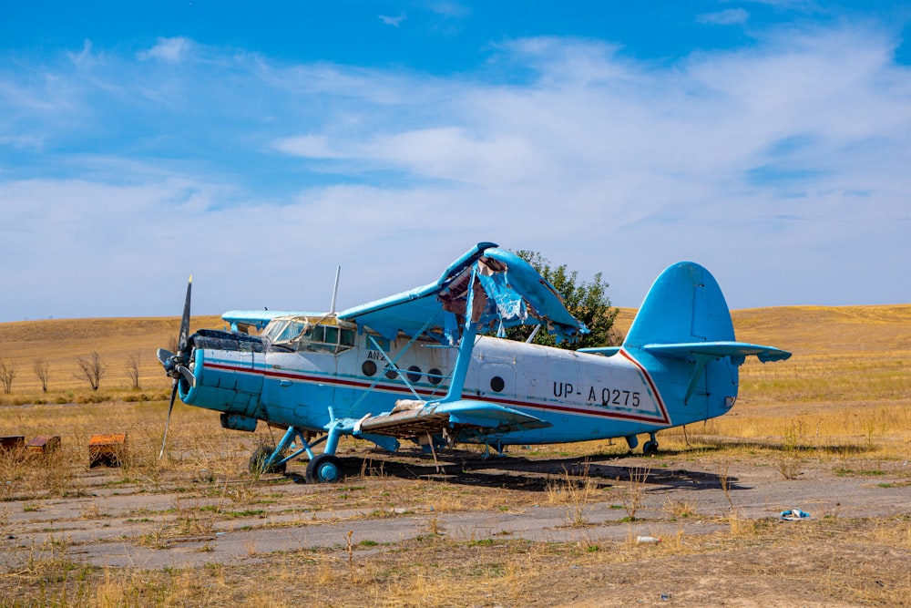 a blue and white airplane sitting on top of a dry grass field