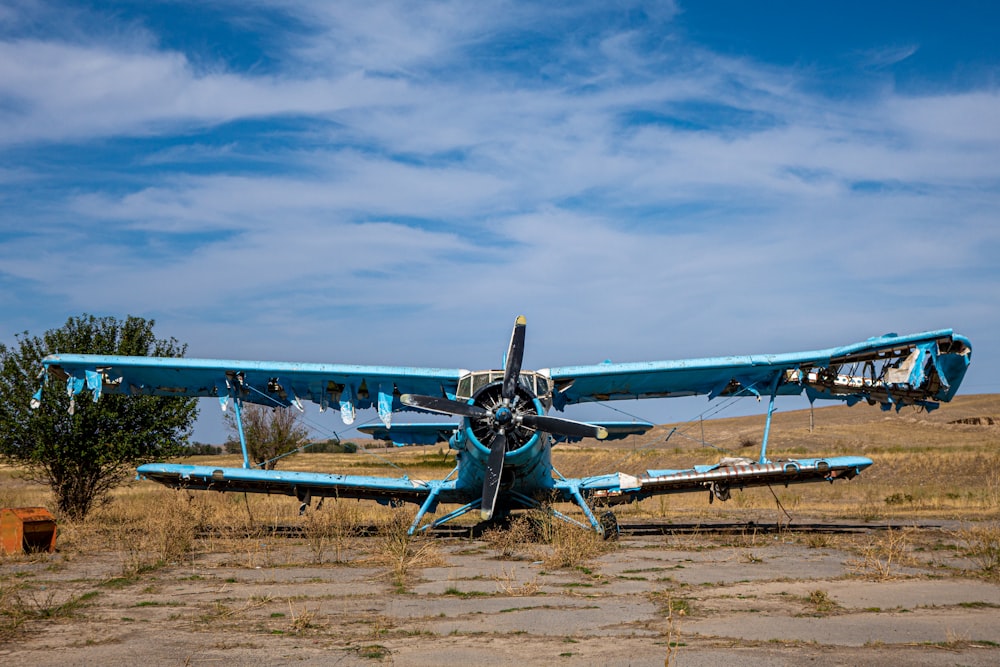 a blue airplane sitting on top of a dry grass field