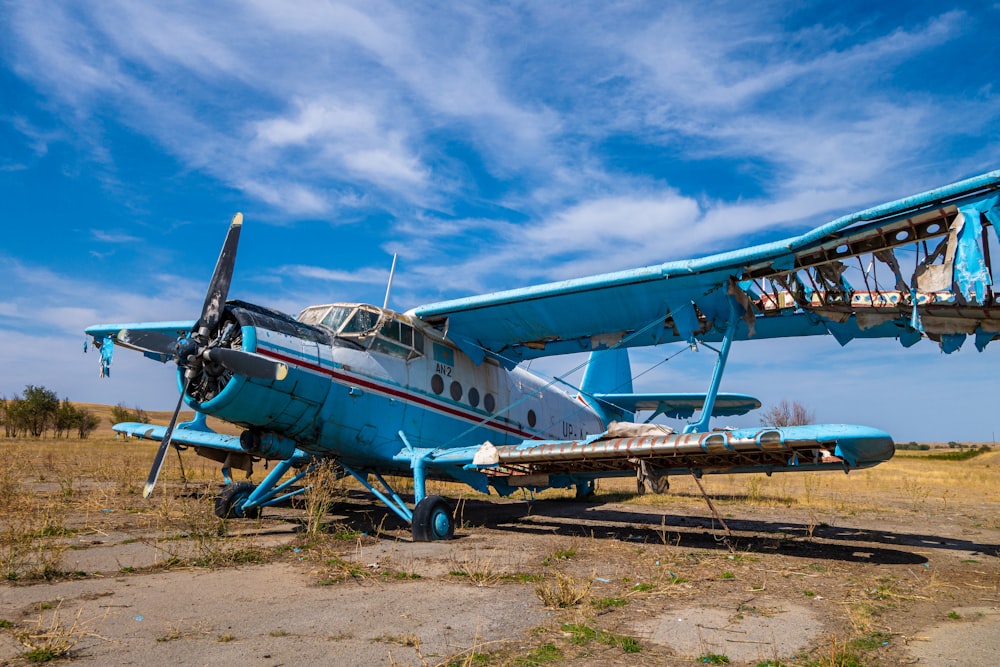a small blue airplane sitting on top of a dirt field