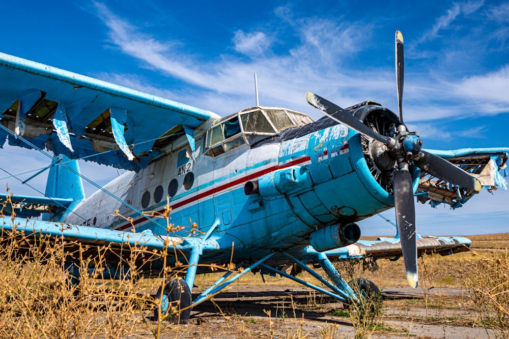 a blue airplane sitting on top of a dry grass field