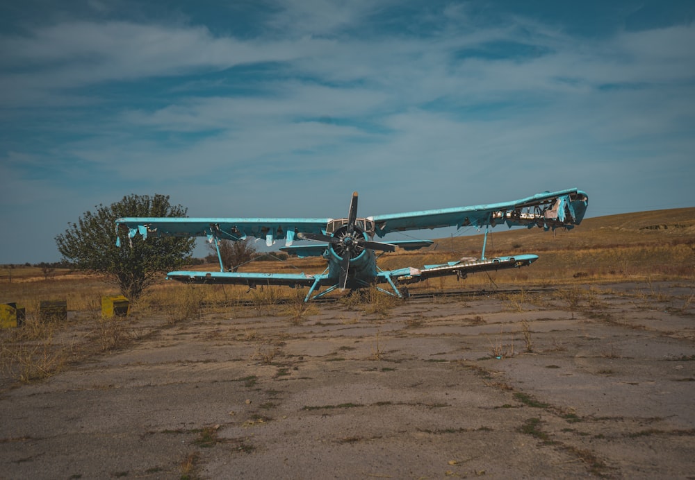 a blue airplane sitting on top of a dry grass field