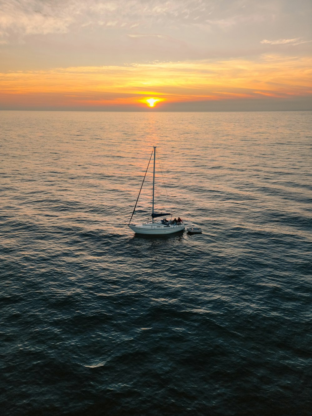 a sailboat in the middle of the ocean at sunset