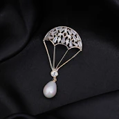 A delicate piece of jewelry shaped like a parachute, adorned with small gemstones and featuring a pear-shaped pearl at the bottom. The jewelry is set against a black, silky fabric background that enhances its luxurious appearance.