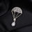 A delicate piece of jewelry shaped like a parachute, adorned with small gemstones and featuring a pear-shaped pearl at the bottom. The jewelry is set against a black, silky fabric background that enhances its luxurious appearance.