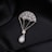 A delicate piece of jewelry shaped like a parachute, adorned with small gemstones and featuring a pear-shaped pearl at the bottom. The jewelry is set against a black, silky fabric background that enhances its luxurious appearance.