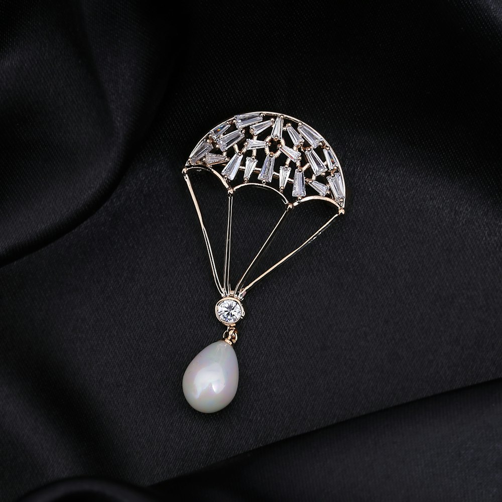a brooch with a pearl hanging from it