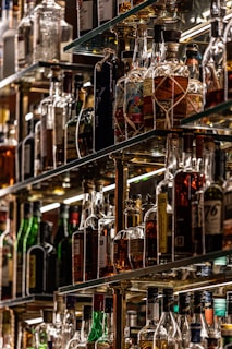 Rows of assorted premium liquors lined up on a backlit shelf, showcasing rich colors and textures.