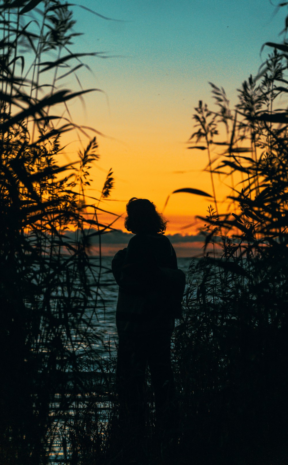 a person standing in front of a body of water at sunset