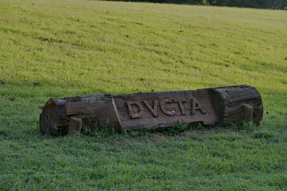a wooden sign sitting in the middle of a lush green field