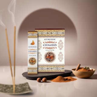 Boxes of Ayurvedic cinnamon masala incense are artfully displayed with intricate patterns and a central image of cinnamon sticks. Nearby, incense sticks emit gentle smoke, while bowls of ground cinnamon and loose sticks are arranged alongside nutmeg and star anise, set against a soft, neutral background.
