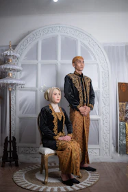 A stylish couple dressed in matching black and gold boubous, smiling confidently against a minimalist backdrop.