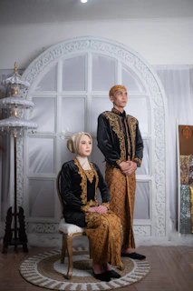 A stylish couple dressed in matching black and gold boubous, smiling confidently against a minimalist backdrop.