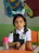 A smiling young girl sitting at a desk with colorful math workbook pages spread out in front of her.