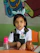 A smiling young girl sitting at a desk with colorful math workbook pages spread out in front of her.