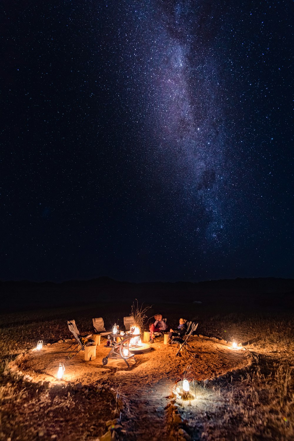 a group of people sitting around a campfire under a night sky filled with stars