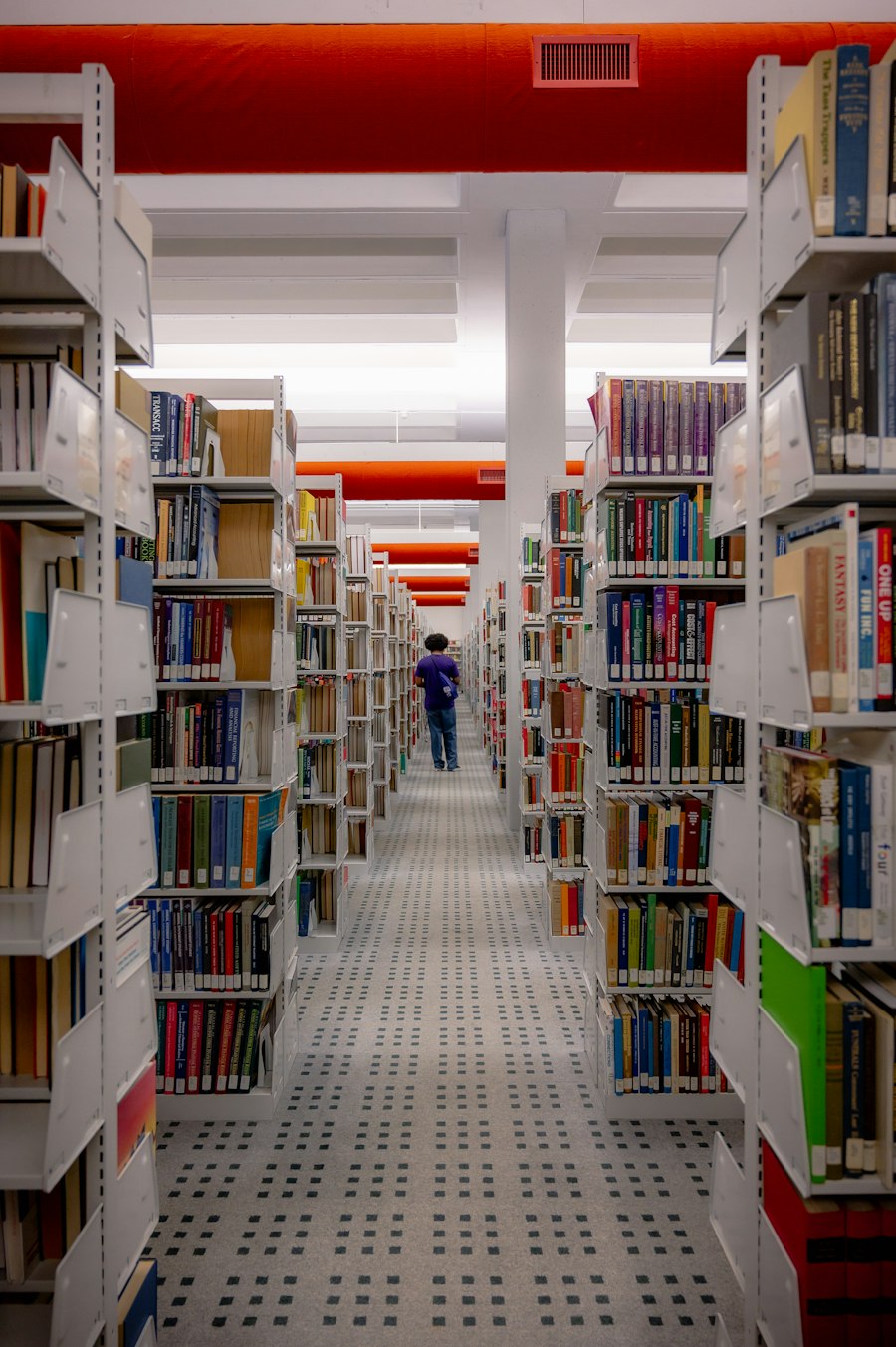 Student walking down a long aisle of library shelves