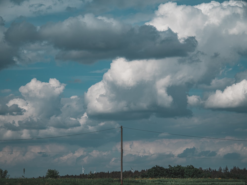 a field with a telephone pole in the foreground and clouds in the background