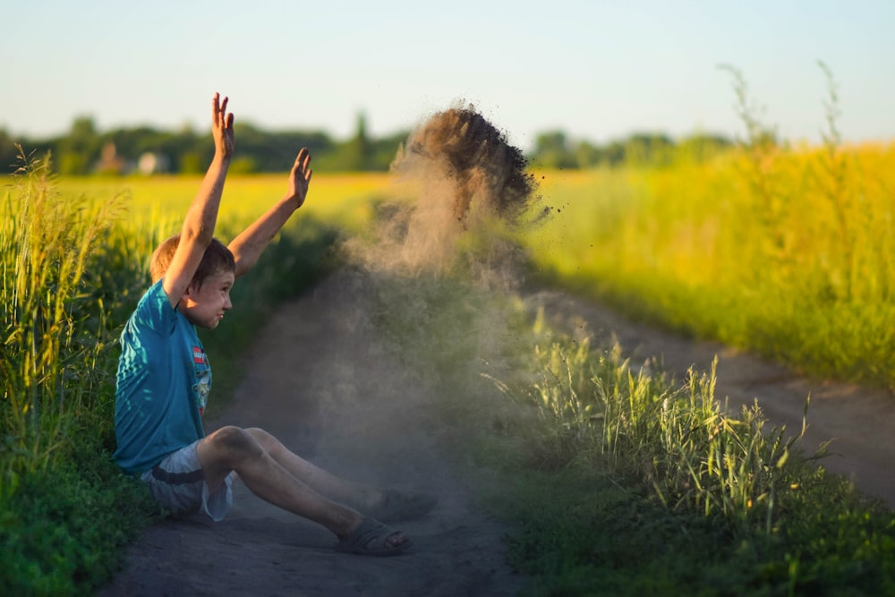 a young boy sitting on the side of a dirt road