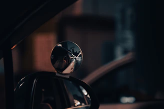 Set of sporty side mirrors mounted on a matte dark blue car, reflecting city lights at night